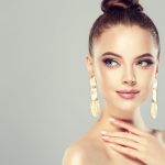 Beautiful model girl with pink manicure on nails . Fashion makeup and cosmetics . Big golden shine earrings jewelry .