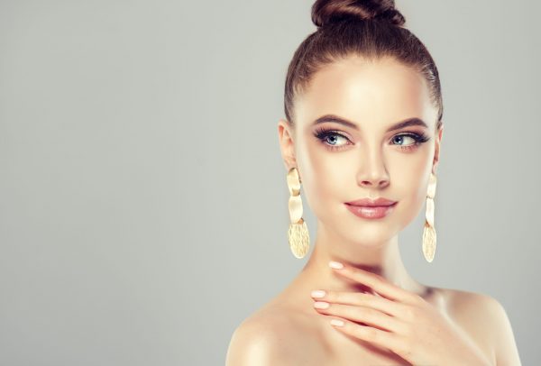 Beautiful model girl with pink manicure on nails . Fashion makeup and cosmetics . Big golden shine earrings jewelry .